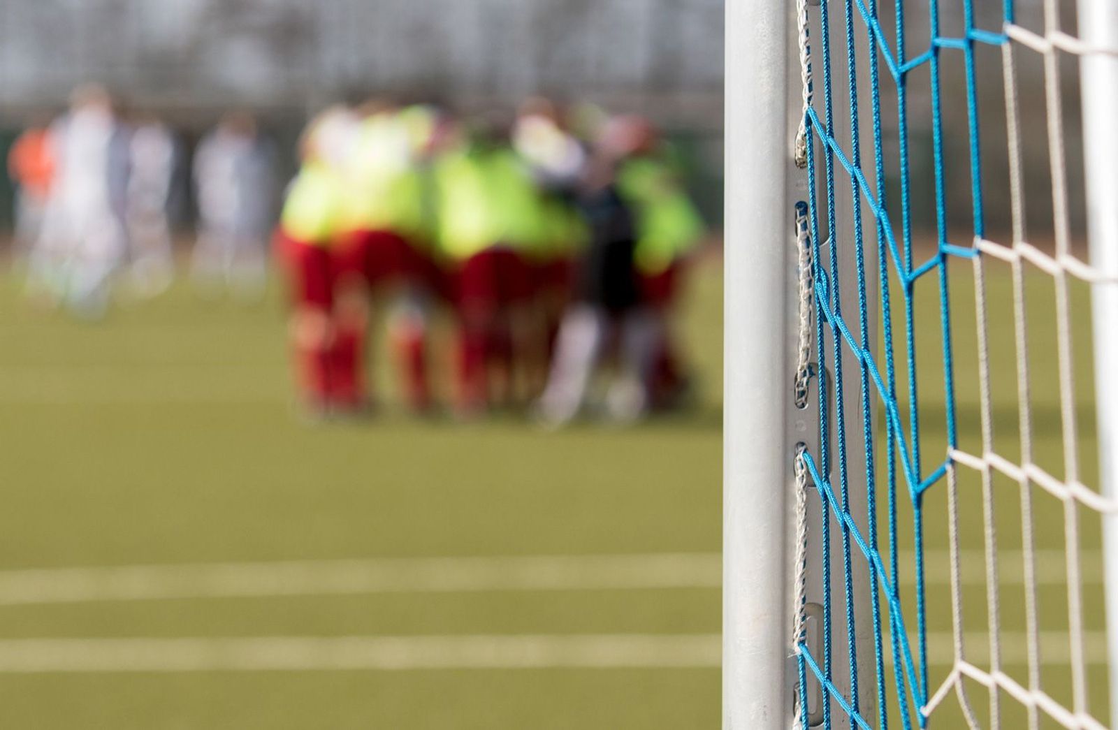 Fußballtor fokussiert auf einem Fußballplatz mit einer Mannschaft unscharf im Hintergrund