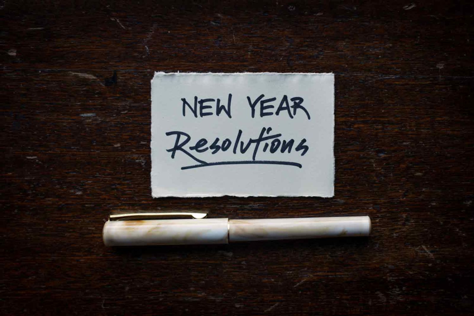 Zettel auf Holztisch mit "New Year Resolutions" und weißem Stift