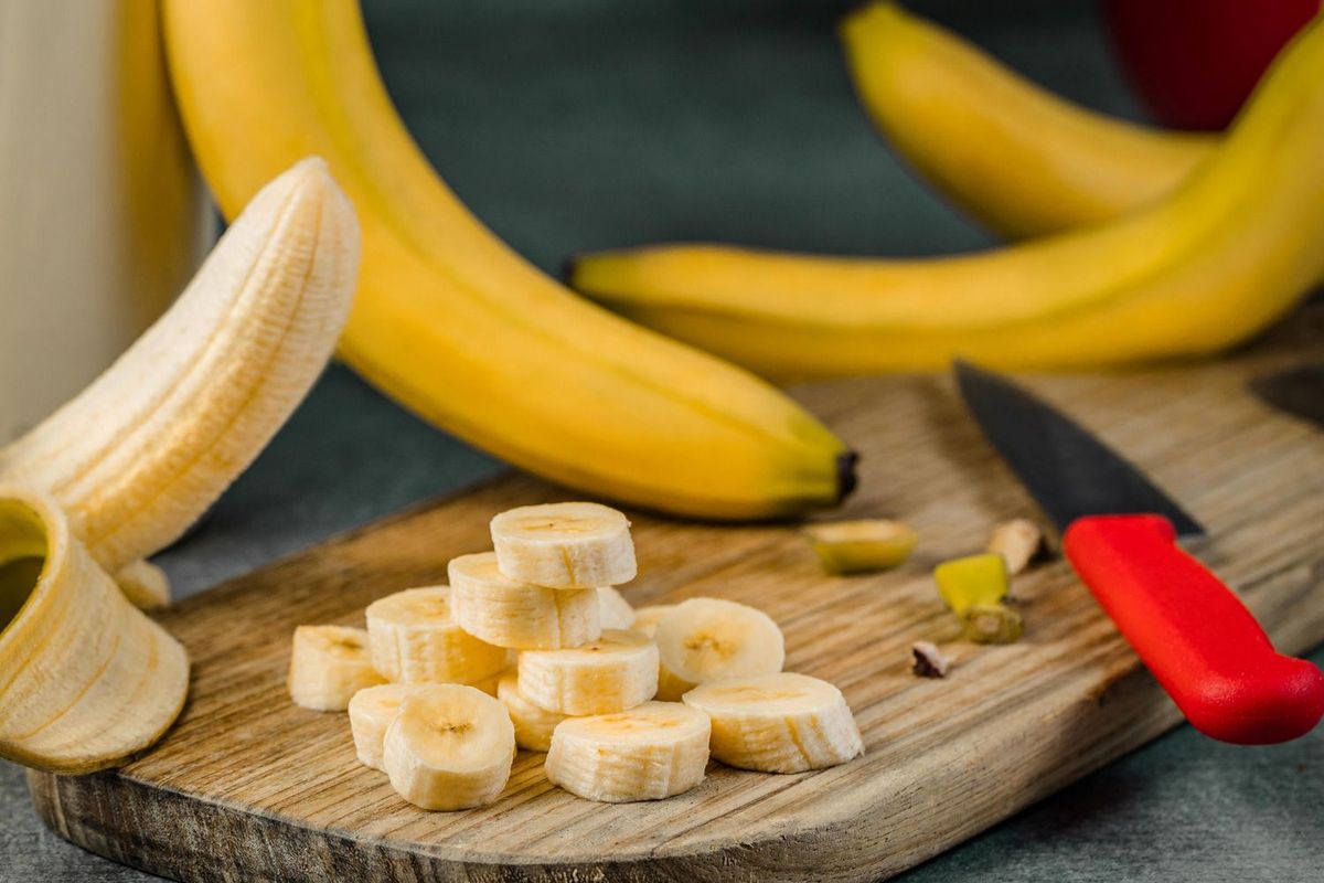 Bananen und geschnittene Banane auf einem Holzbrett mit rotem Messer