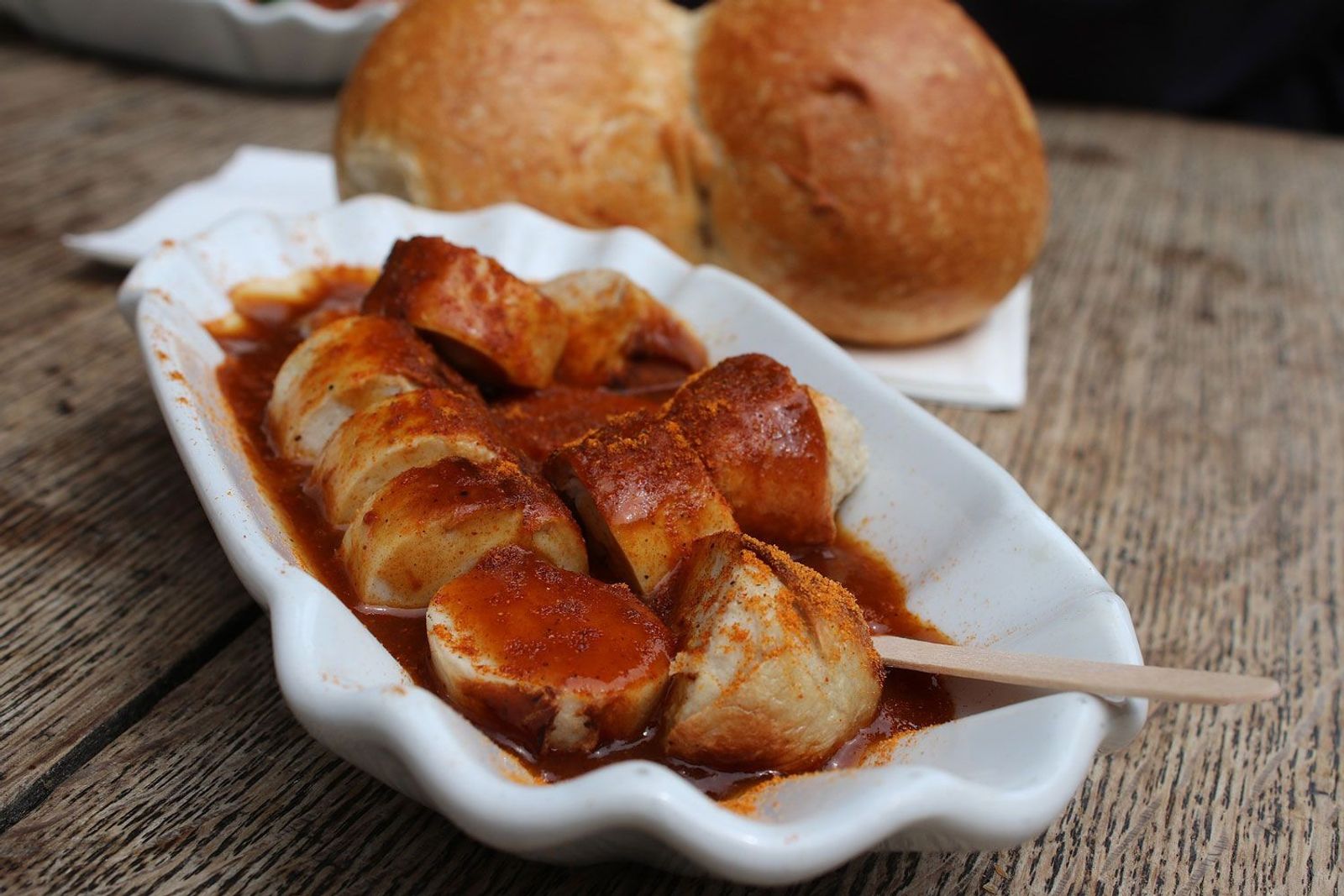 Dutch Oven Currywurst in Schale mit Picker auf einem Holztisch und Brötchen