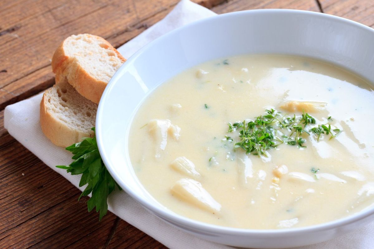 Teller mit Spargelcremesuppe aus dem Feuertopf mit Baguette und Kresse auf Holztisch