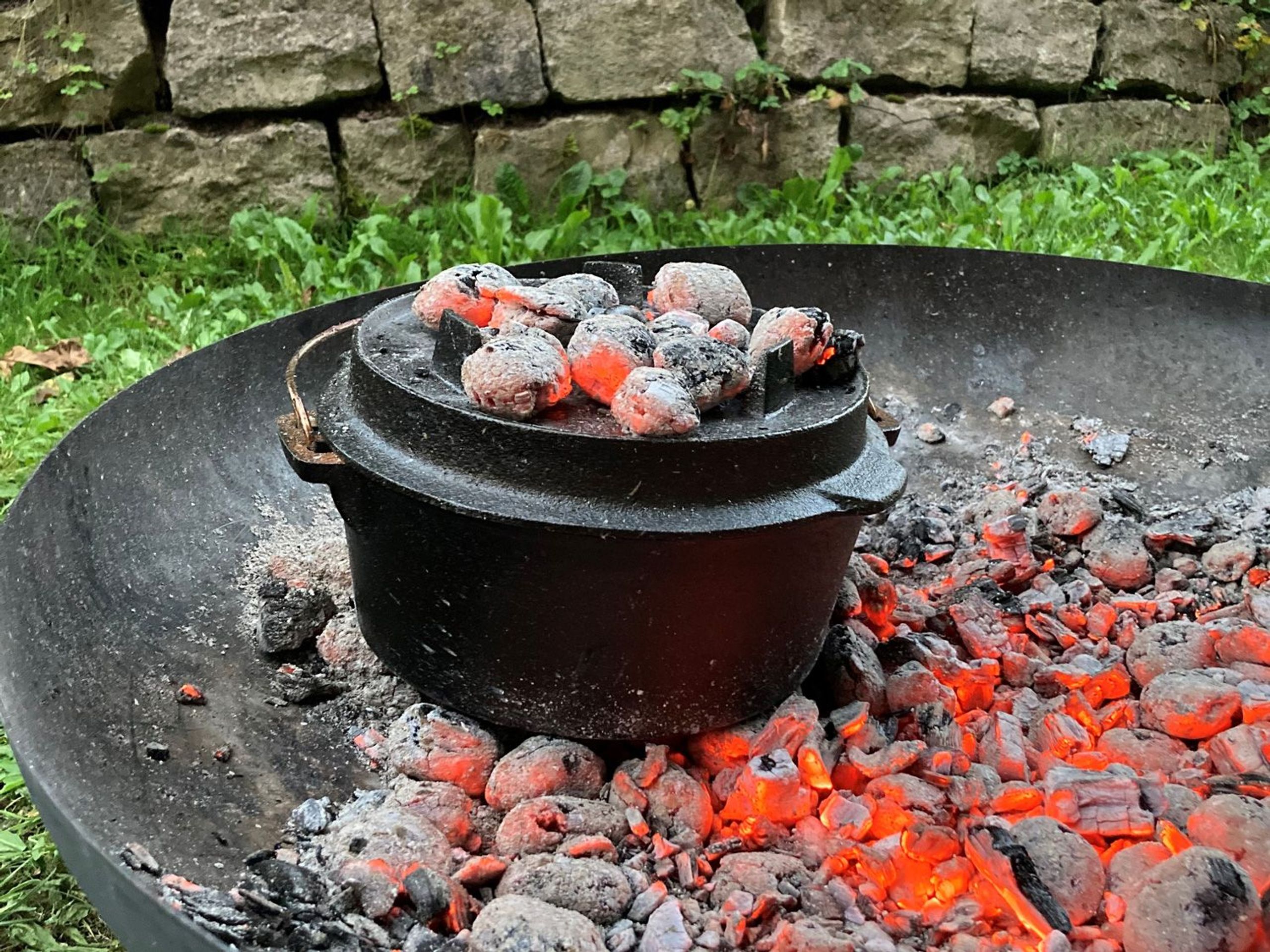 Dutch Oven mit Deckel, auf denen Briketts liegen in Feuerschale mit Briketts