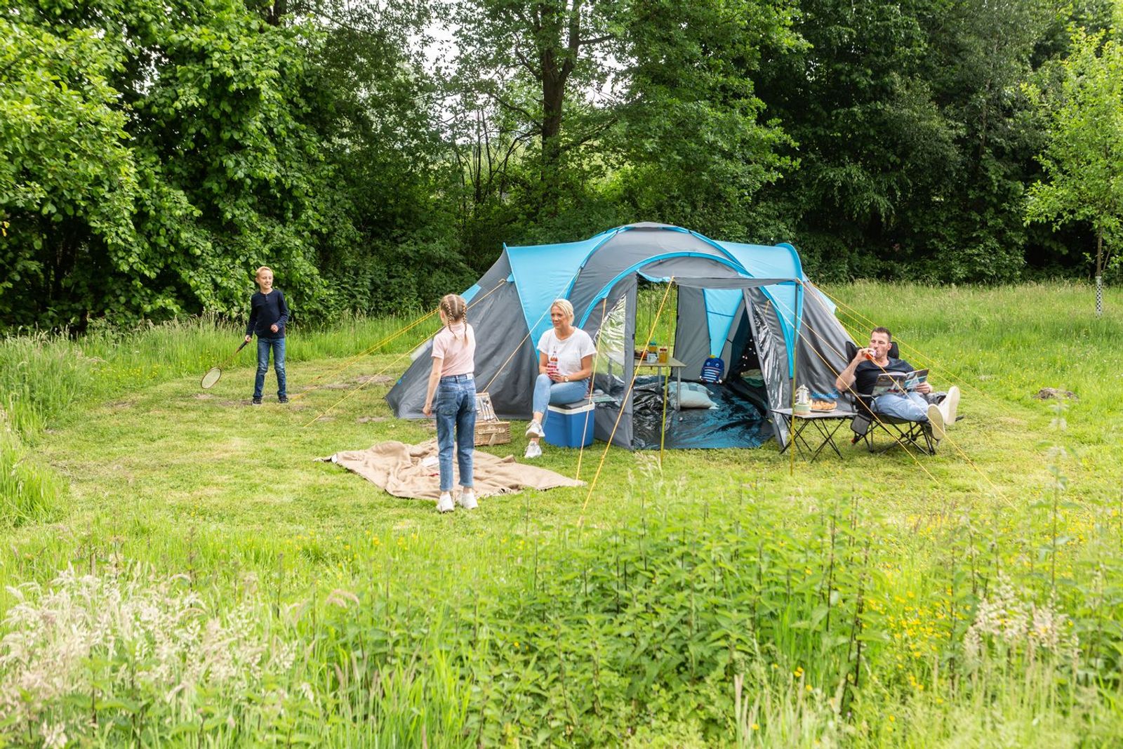 Familie beim Camping auf einer Wiese mit Bäumen im Hintergrund