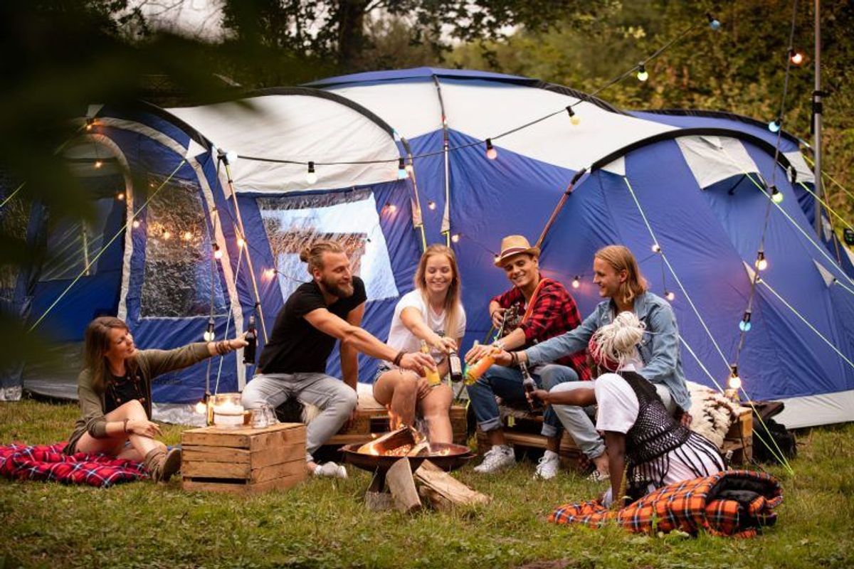 Freundesgruppe am Lagerfeuer vor blauem Campingzelt Nimbus 12 in der Dämmerung