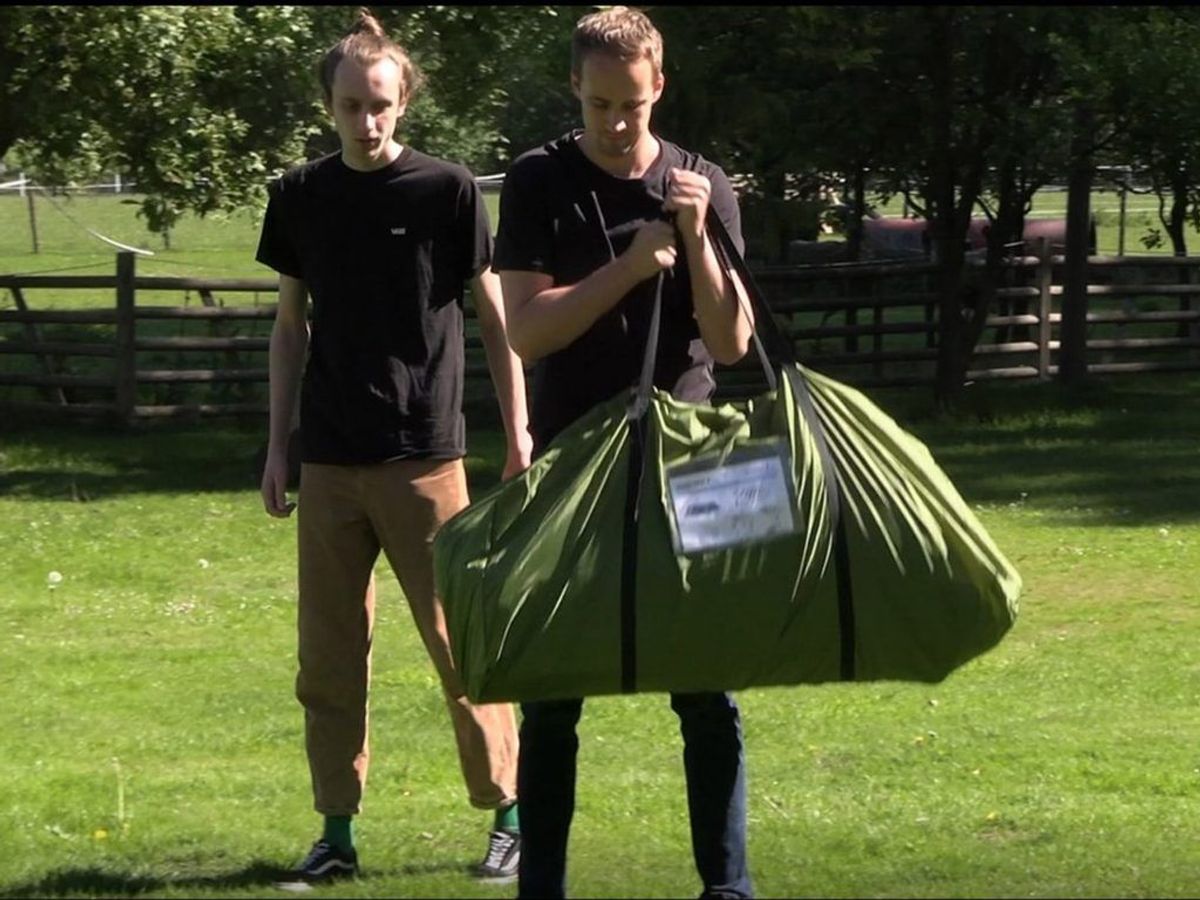 Eingepacktes Gruppenzelt Skandika Montana 10 Sleeper Protect getragen von einer Person mit einer weiteren Person im Hintergrund