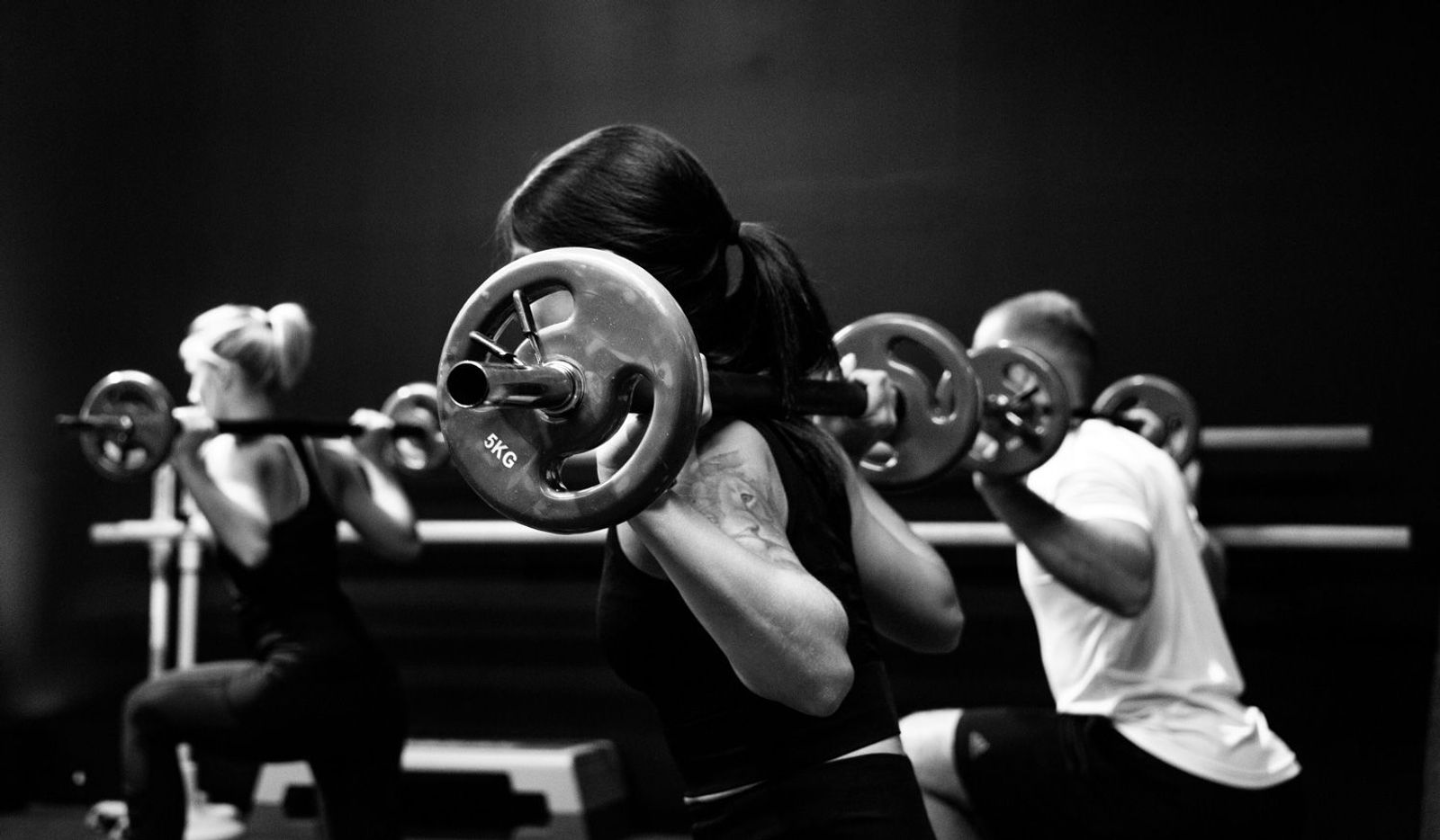 Frau beim Langhanteltraining mit anderen Sportlern