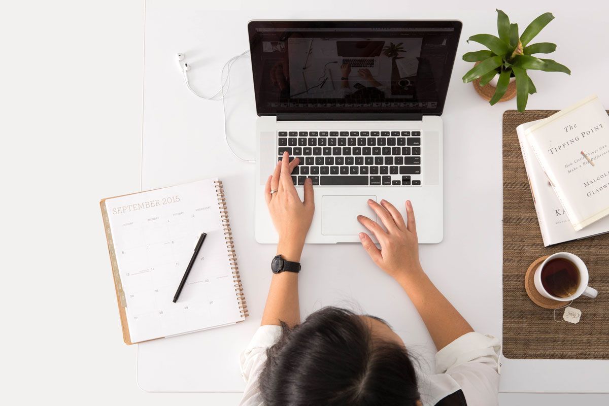 Frau am Laptop am Tisch sitzend von oben fotografiert mit Terminplaner und einer Tasse Tee