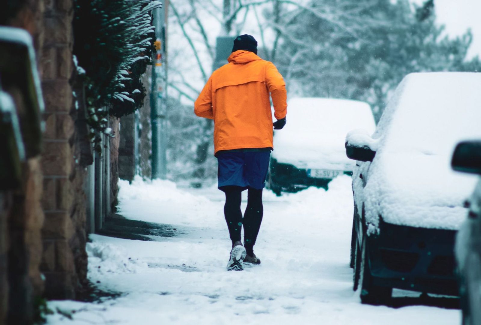 Jogger mit orangener Jacke an einer verschneiten Straße