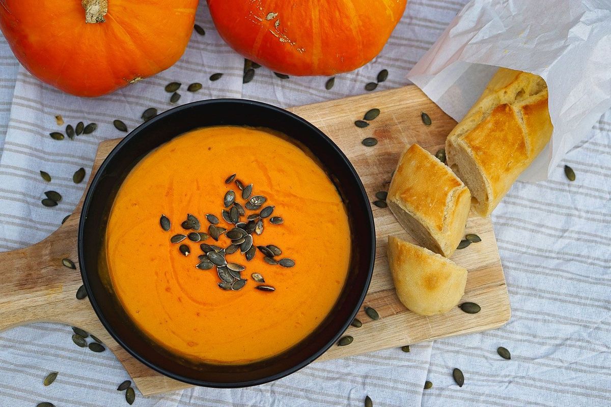 Kürbissuppe aus dem Dutch Oven serviert mit Kürbiskernen und Baguette