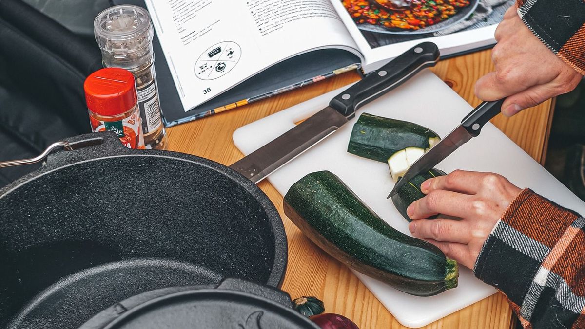 Tisch mit Schneidebrettchen und Person, die eine Zucchini schneidet