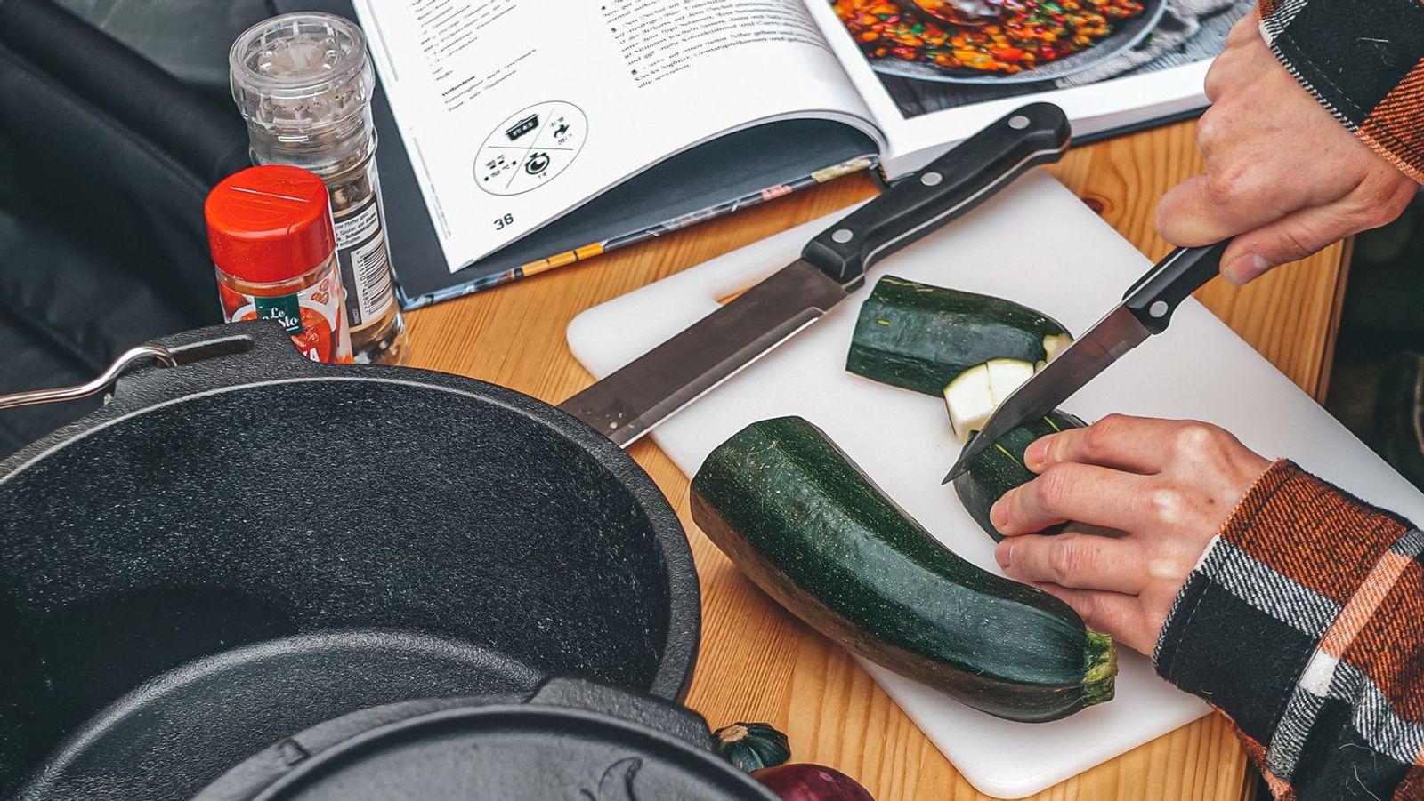 Tisch mit Schneidebrettchen und Person, die eine Zucchini schneidet