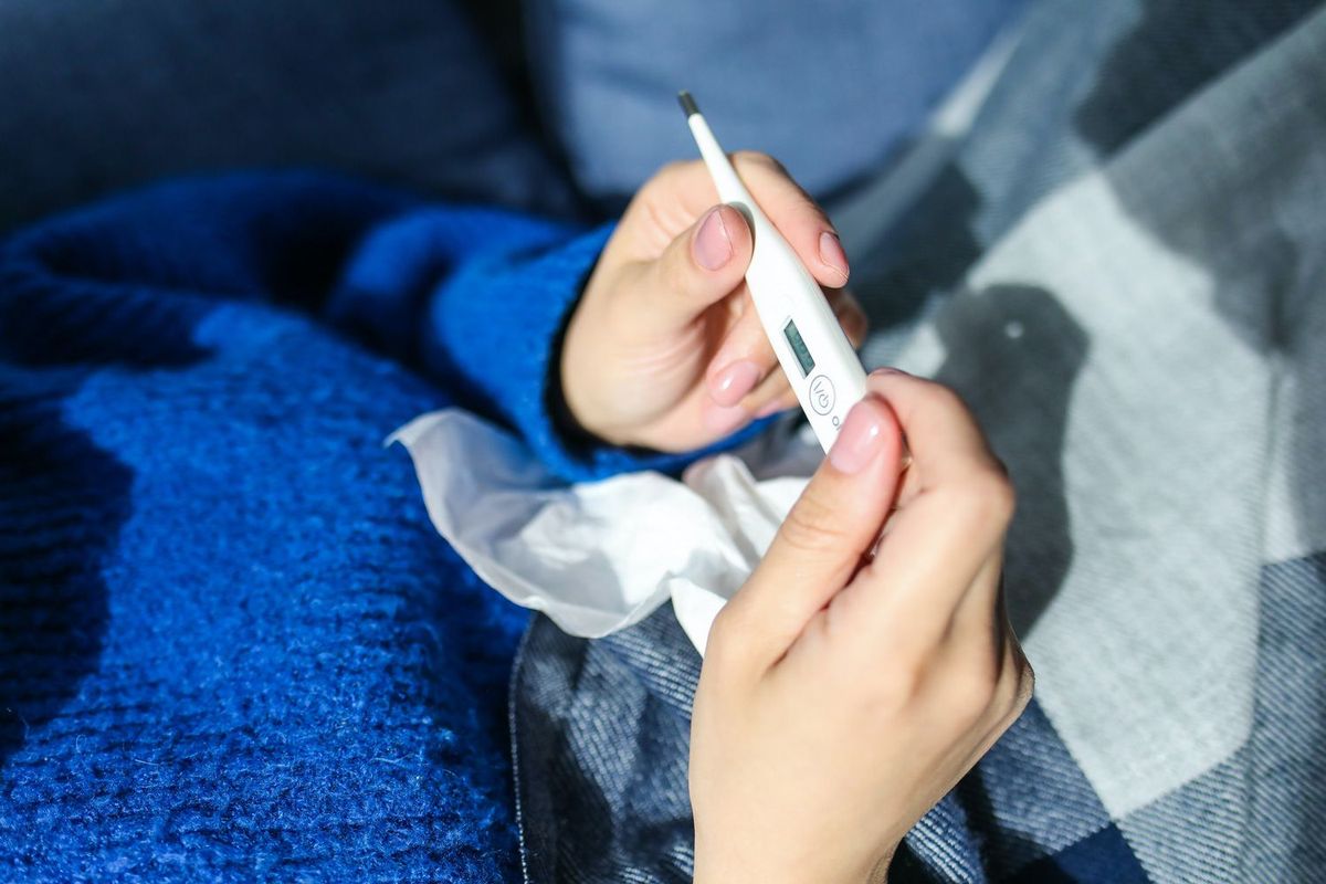 Frau mit Fieberthermometer in der Hand und Taschentuch