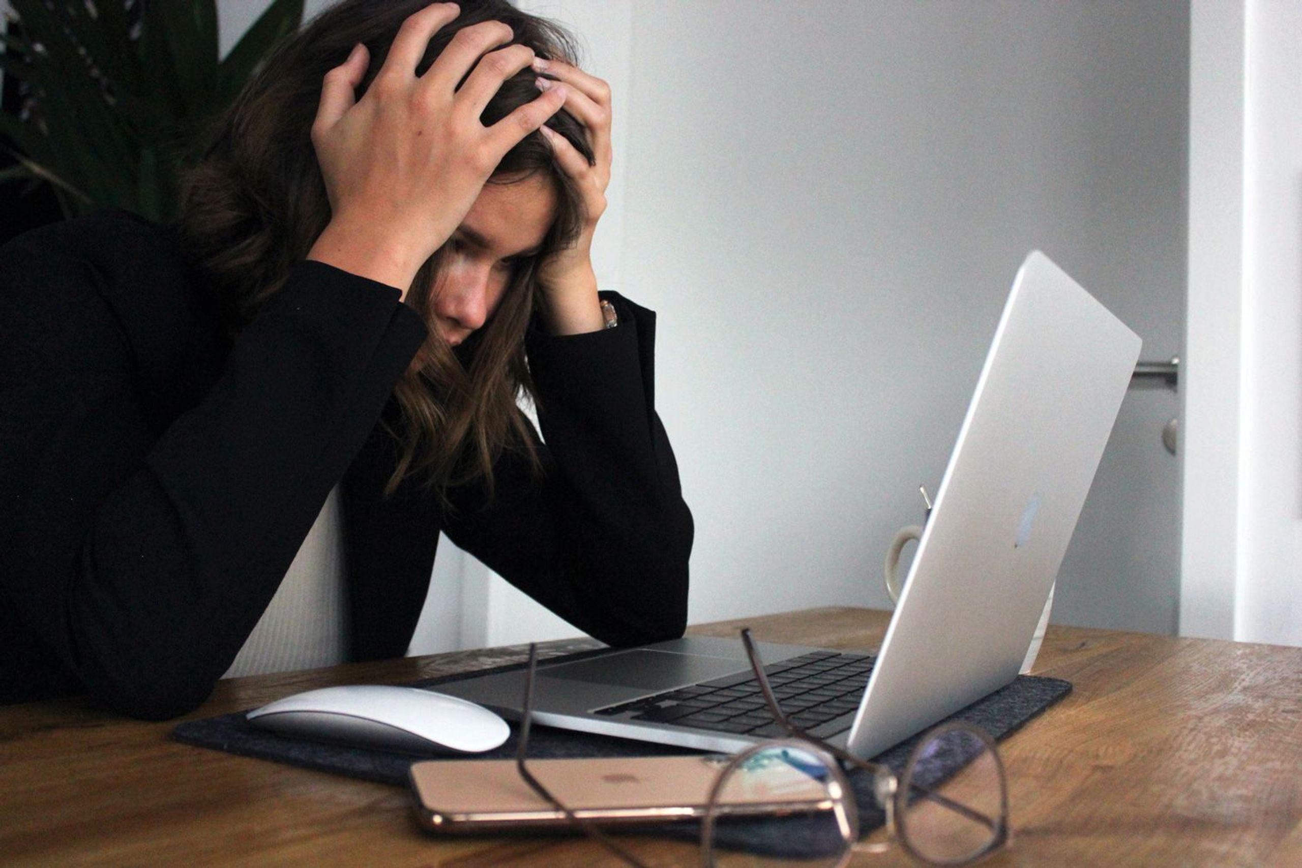 Gestresste Frau am Schreibtisch mit Laptop und Brille daneben liegen