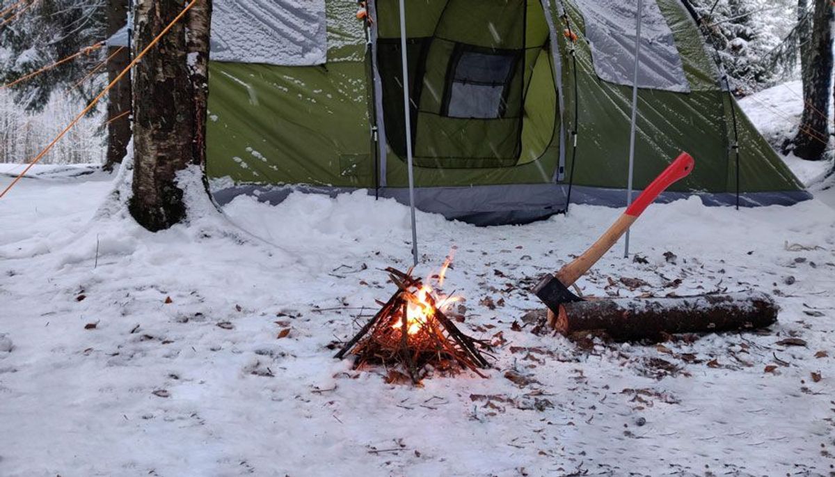 Winterlandschaft mit Lagerfeuer und Zelt im Hintergrund