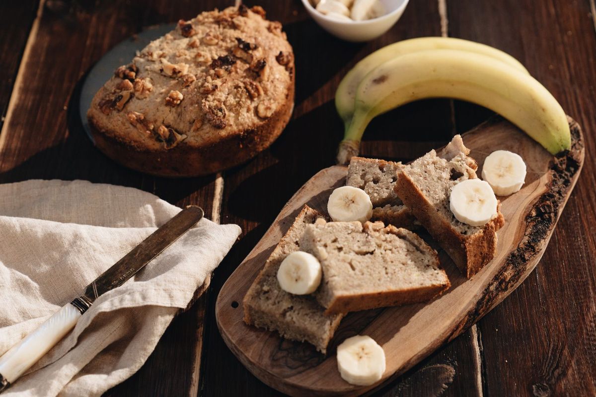 Aufgeschnittenes Bananenbrot auf einem Holzbrett und Banane daneben