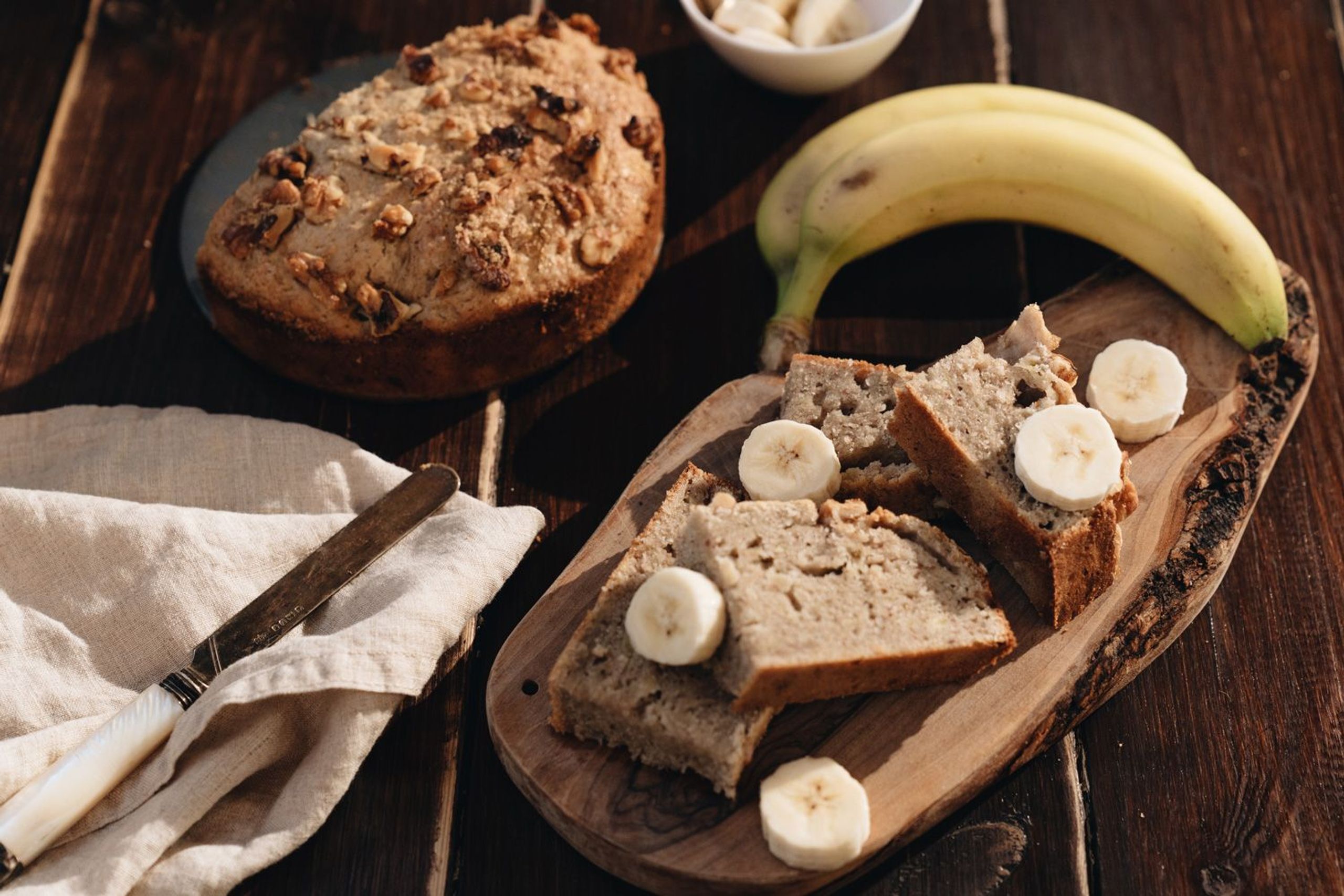 Aufgeschnittenes Bananenbrot auf einem Holzbrett und Banane daneben