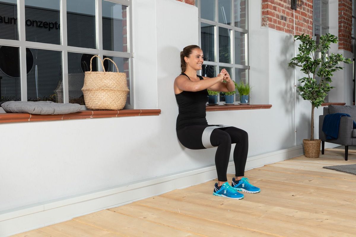 Sportlerin in Kulisse mit Fitnessbändern bei einem Wall Sit