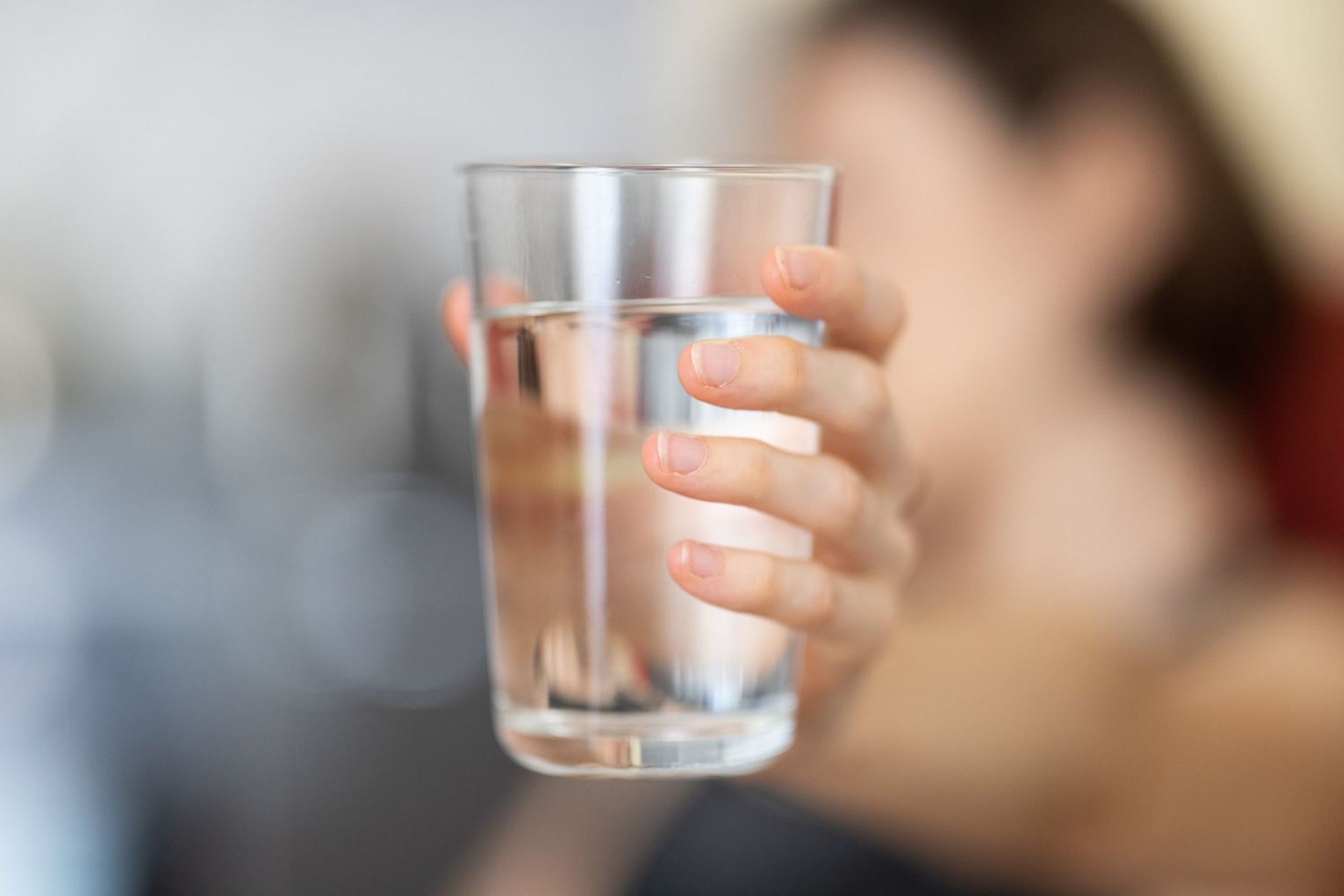 Wasserglas im Fokus mit verschwommener Person im Hintergrund