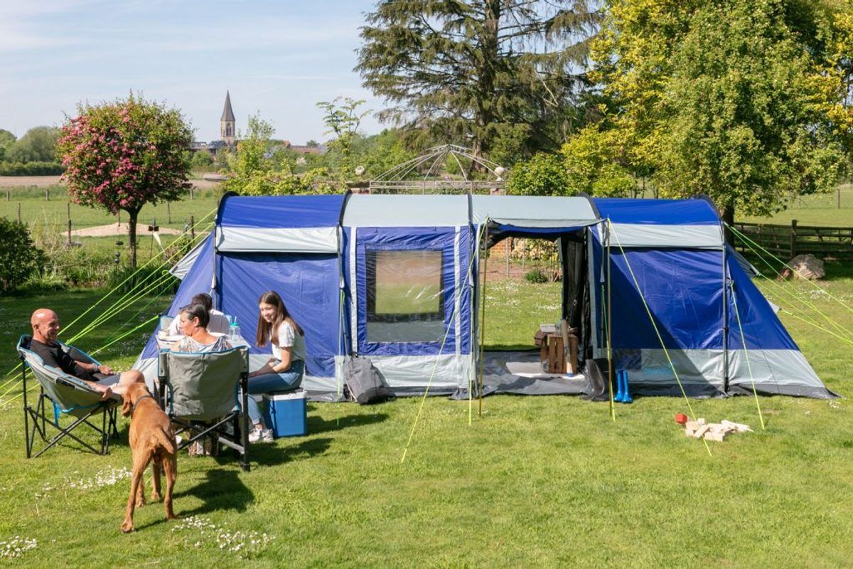 Familie mit Hund, die vor einem Zelt mit Campingstühlen und Tisch sitzt