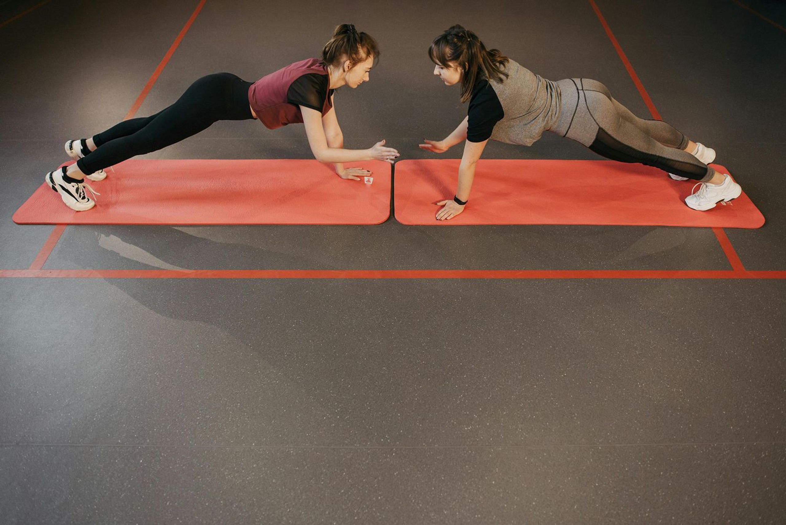 Zwei Sportlerinnen bei Liegestützen mit Abklatschen auf roten Fitnessmatten