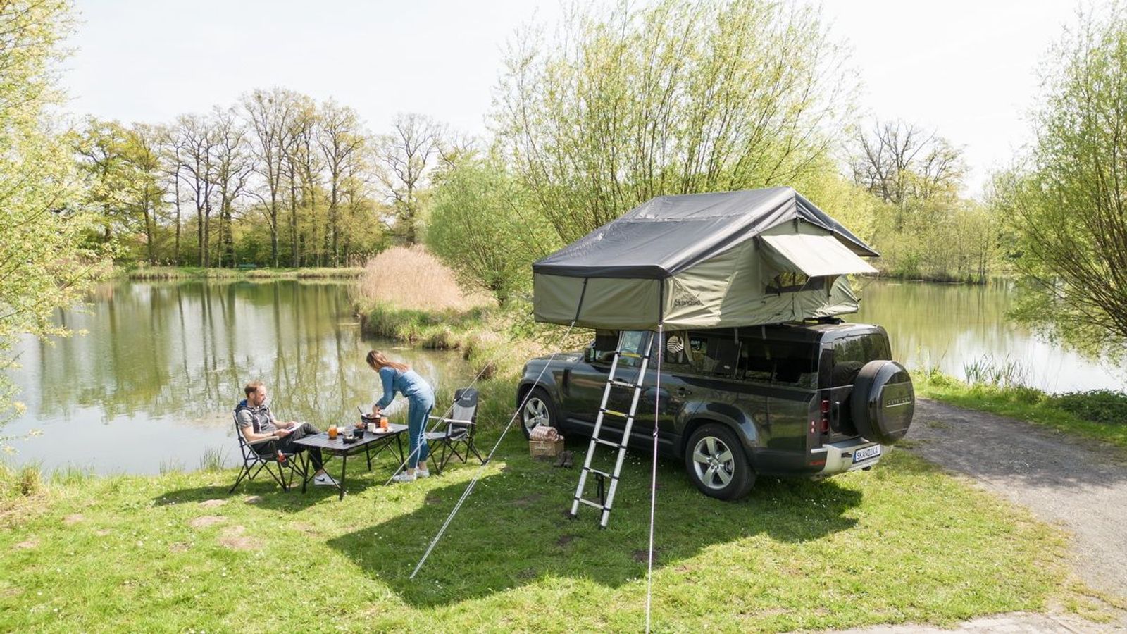 Dachzelt Freeland 3 mit 2 Campern vor dem Auto auf Stühlen