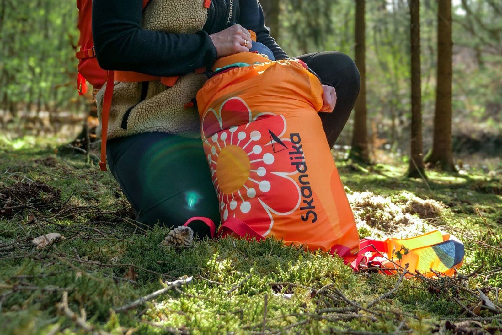 Person, die im Wald einen Sovro Schlafsack mit Blumen auspackt