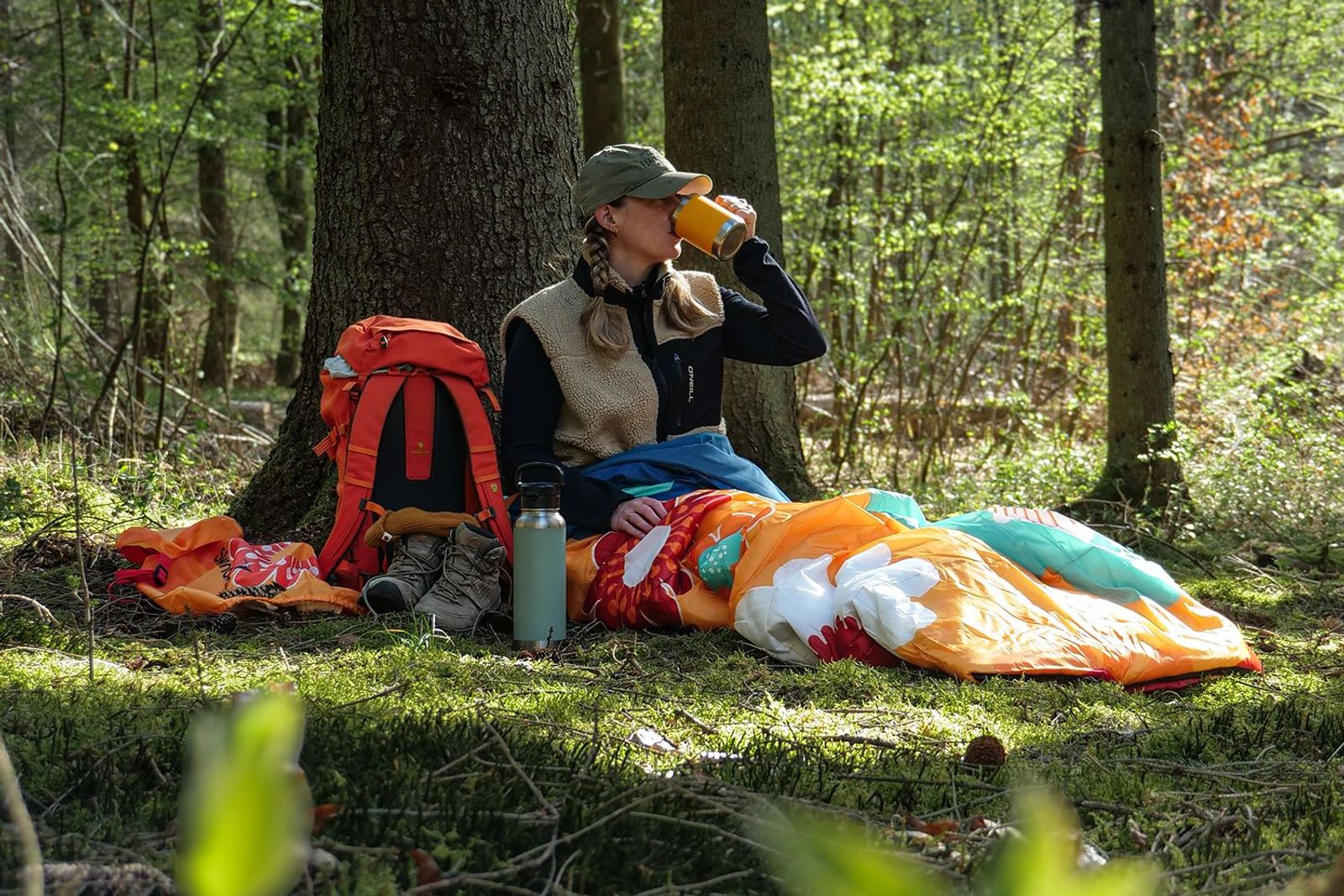 Sovro Schlafsack ausgebreitet auf einem Waldboden mit Frau, die etwas trinkt