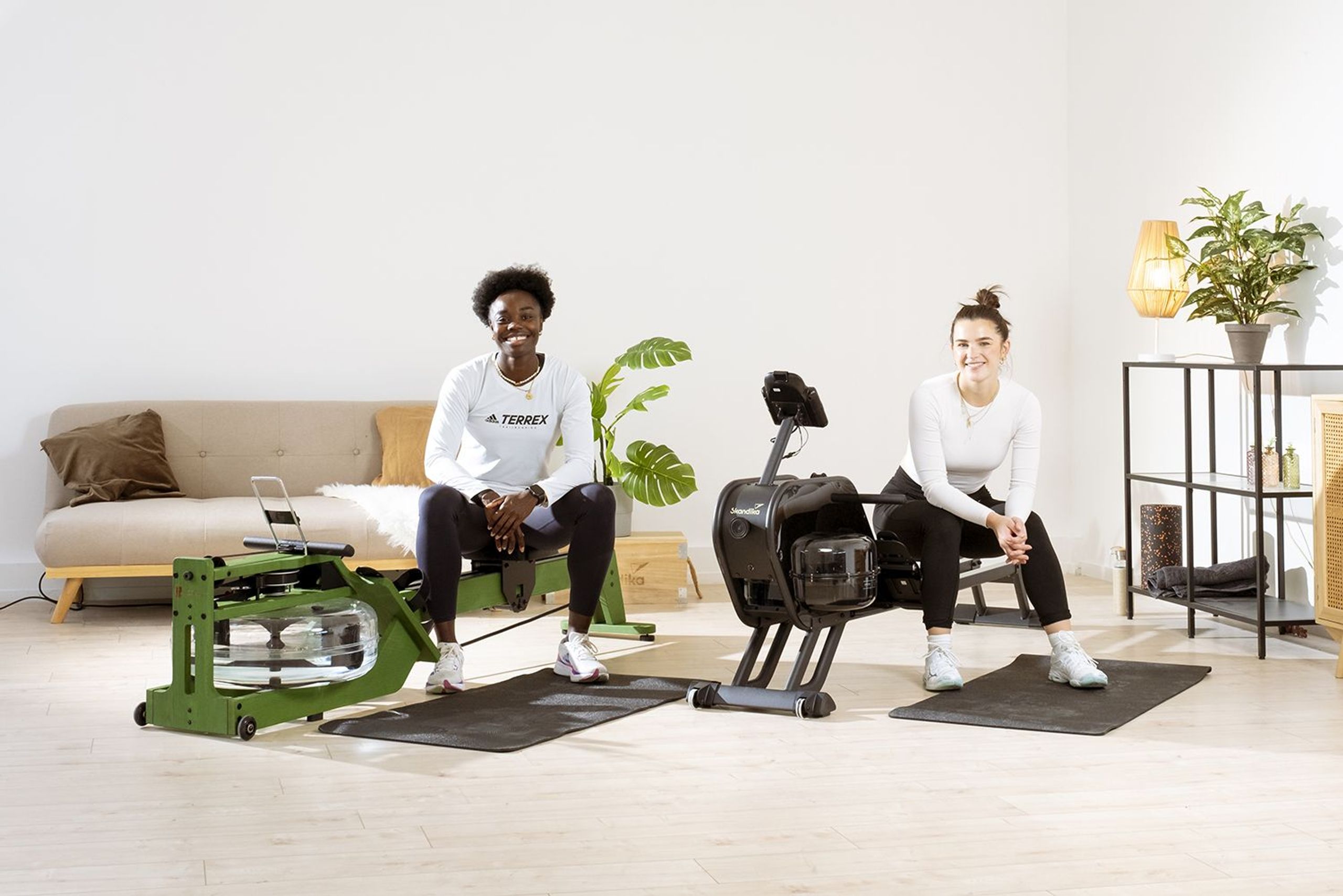 Zwei Sportlerinnen beim gemeinsamen Workout auf zwei Rudergeräten mit Bodenschutzmatte